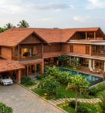 A large two-story modern Kerala-style luxury home featuring exposed red brick walls, traditional sloped terracotta tile roofs, wooden balconies, a private swimming pool, and a landscaped yard set against a lush tropical forest backdrop.